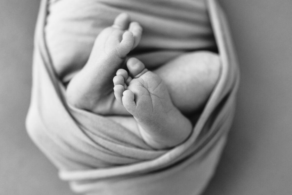 newborn baby swaddled with feet sticking out and toes on display