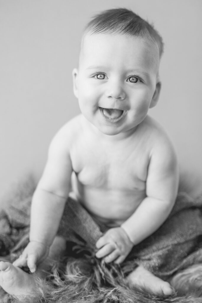 black and white photo of little boy sitting up with wrap across legs and smiling at the camera
