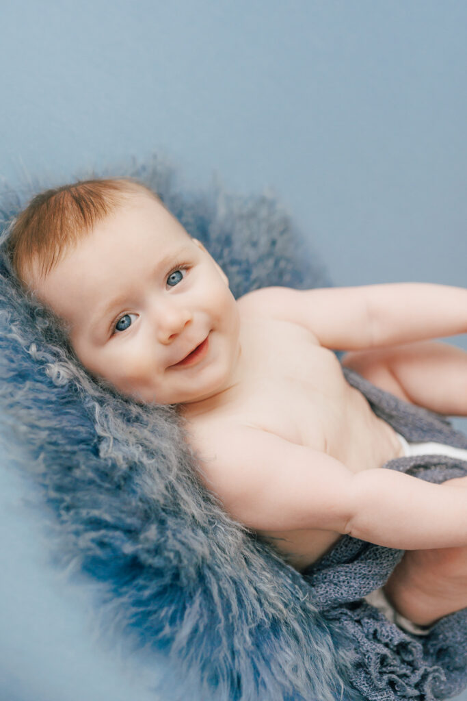 smiling baby boy with blue eyes and blue backdrop