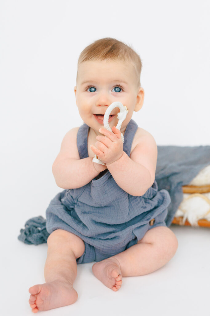 six month old baby boy holding toy on white backdrop sitting