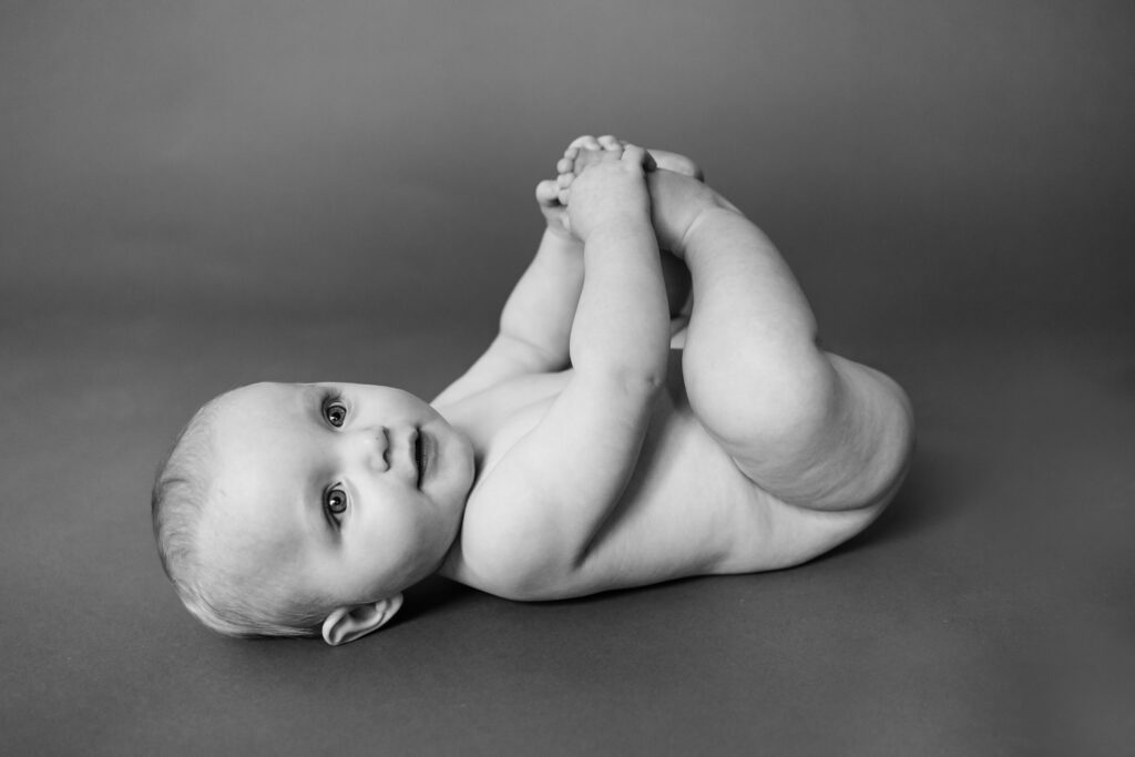 six month old little boy black and white photograph baby on back  without clothes and holding feet smiling