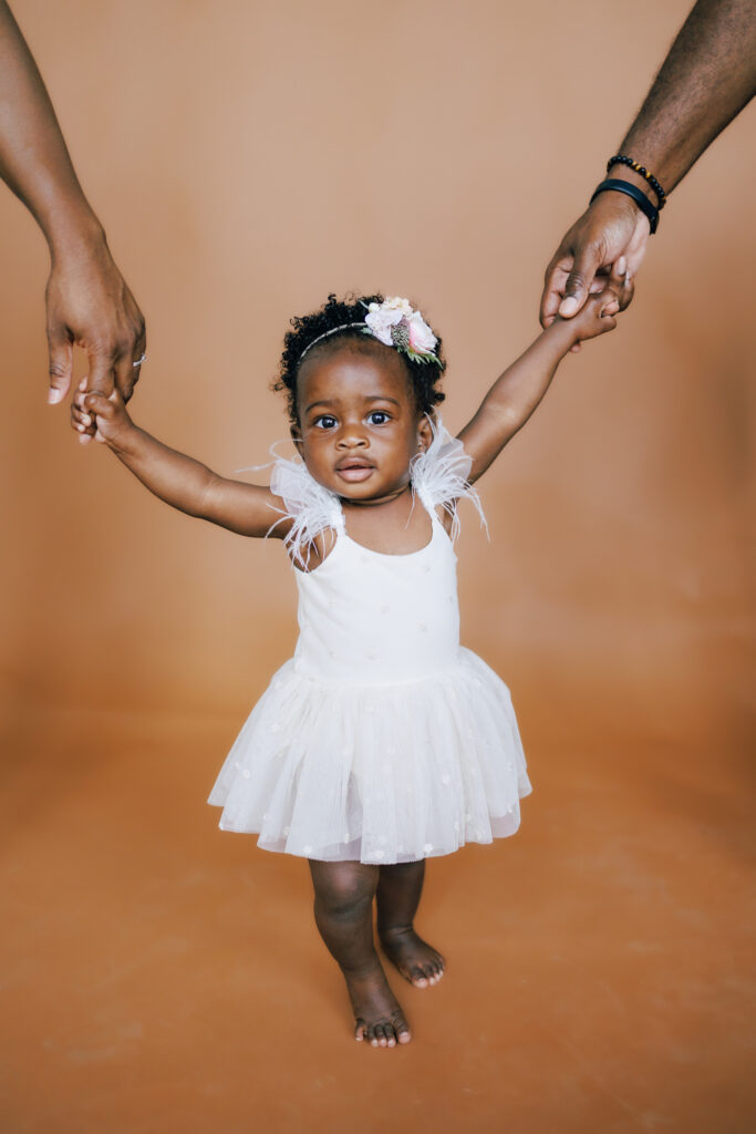 baby girl one year old standing holding mom and dads hands