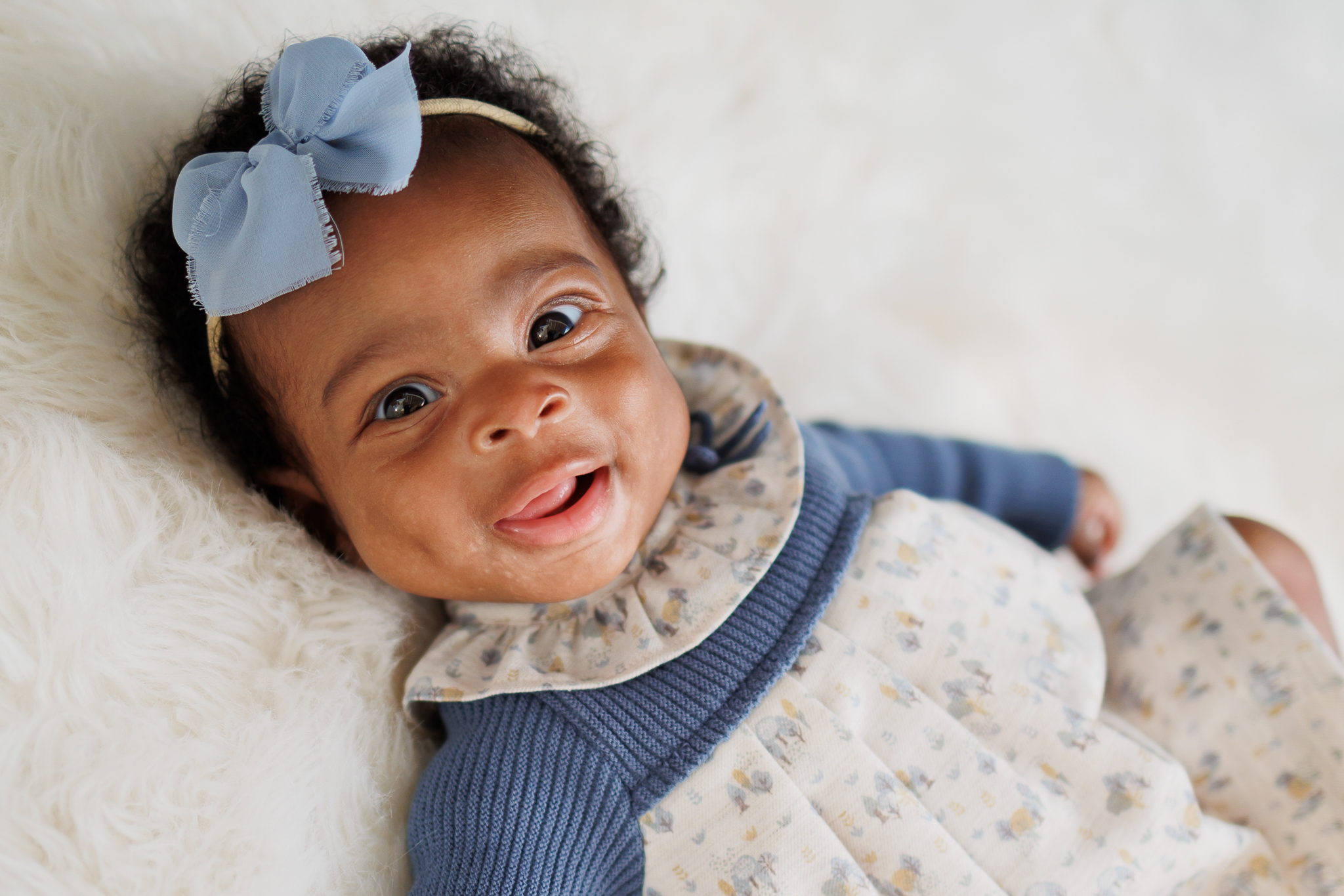 three month old little girl on white backdrop wearing blue bow and dress