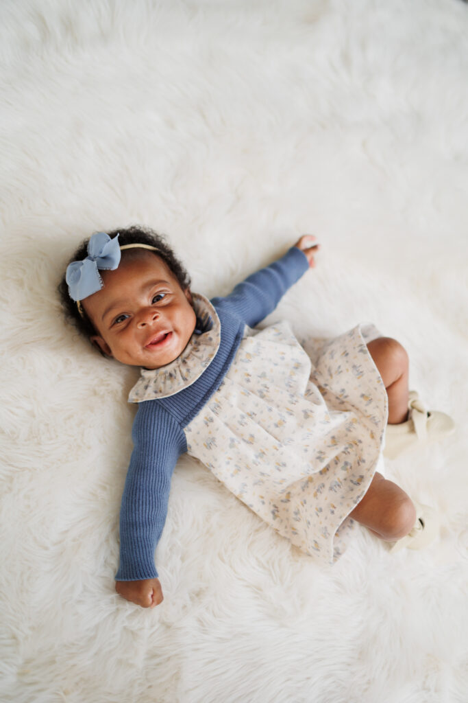 three month old baby girl wearing blue blow and dress against white fur backdrop