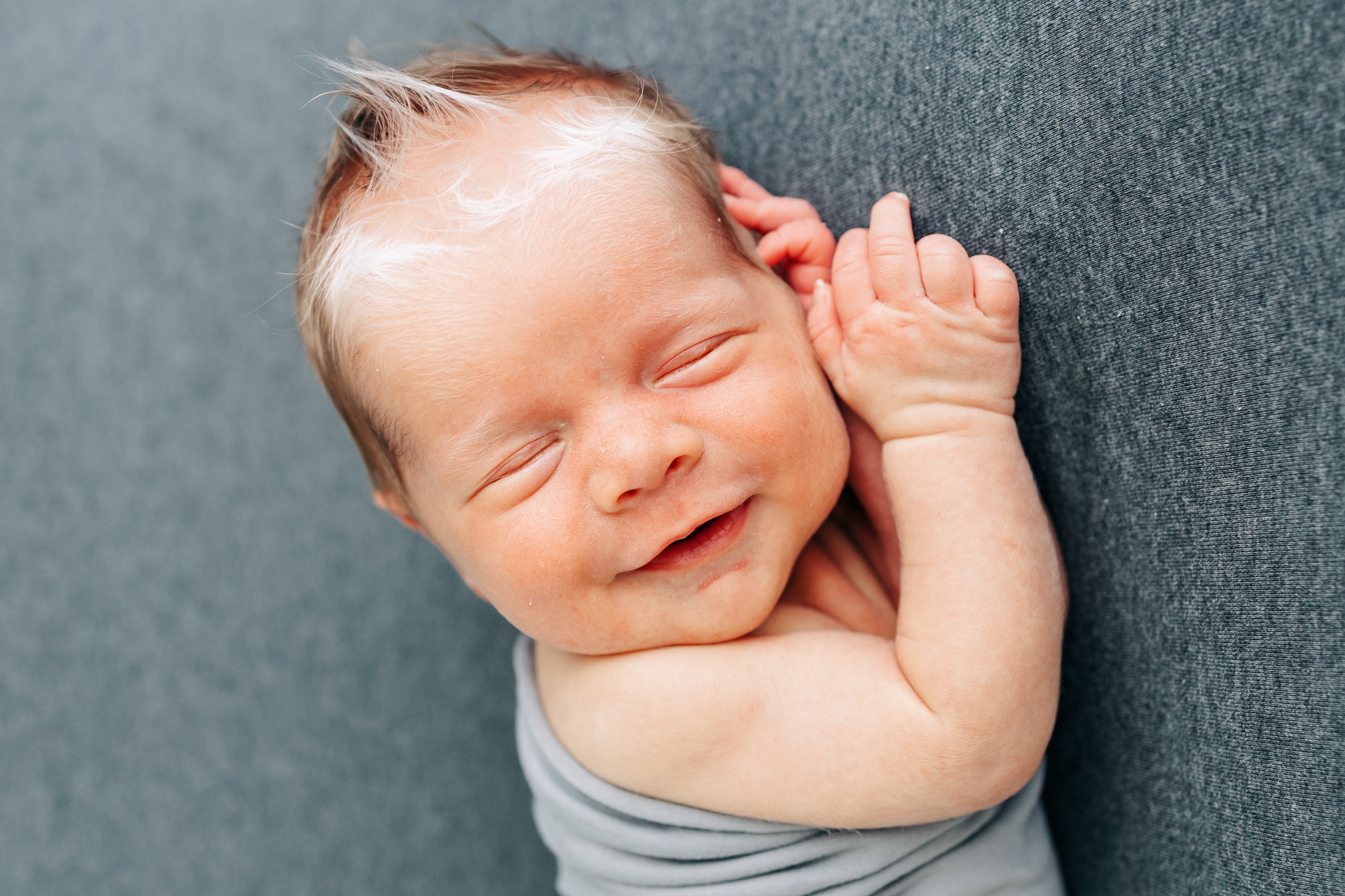 newborn baby boy with white birthmark in hair smiling on gray backdrop Columbus pediatric dentist