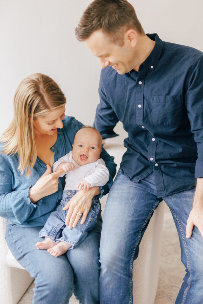 three month old baby boy with mother and father sitting on white chair looking at baby