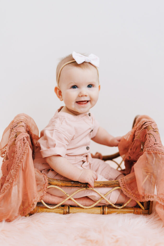six month old baby girl sitting in small wooden crib against white backdrop columbus daycares