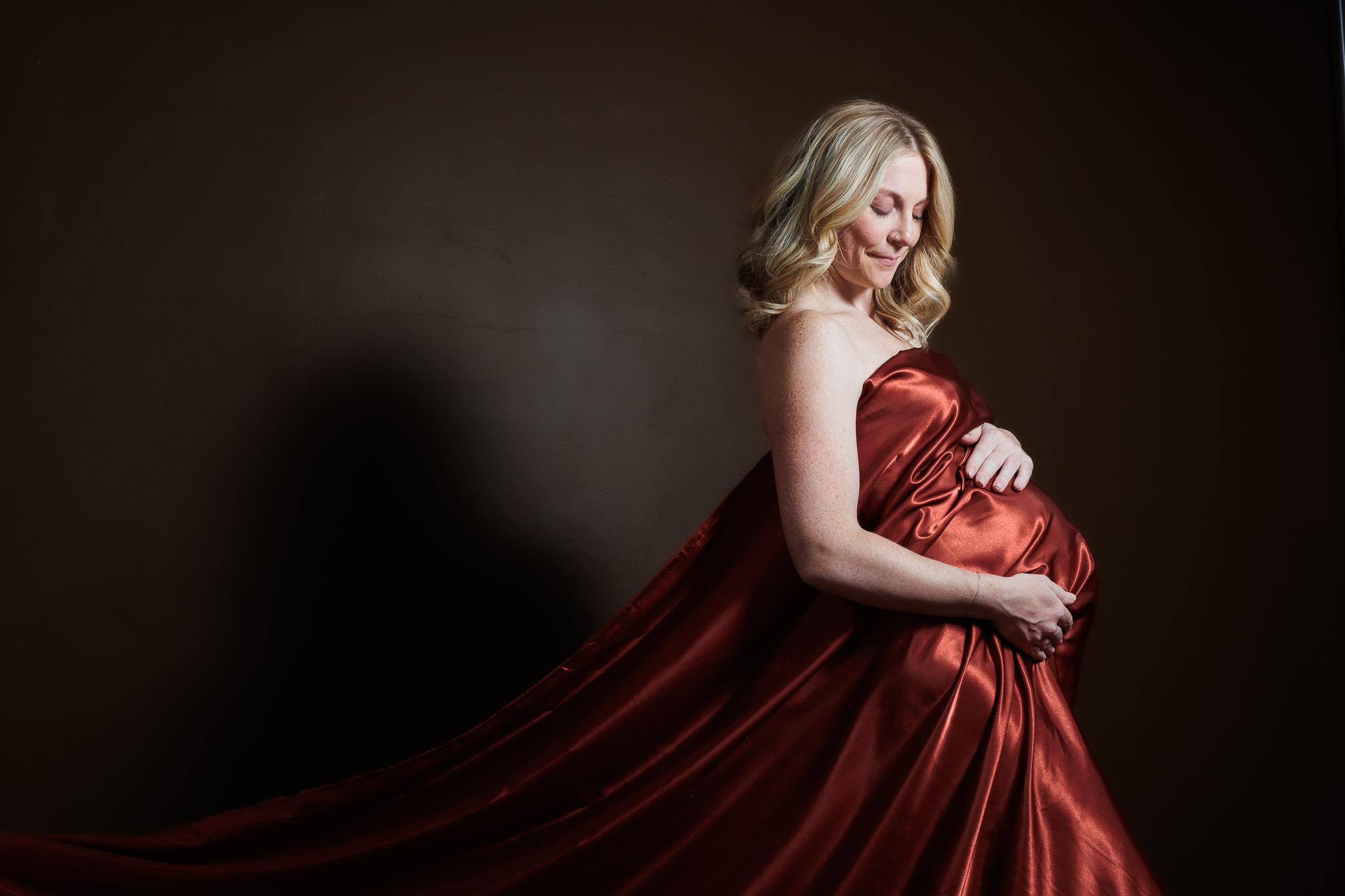 maternity photo shoot with dark background and red fabric draping