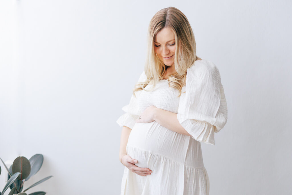 maternity photo shoot with white wall and white gown. 