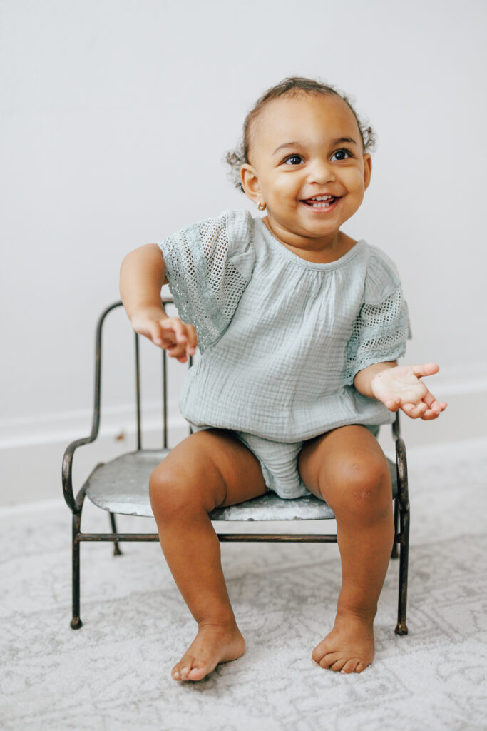 baby girl wearing green romper sitting on wire chair