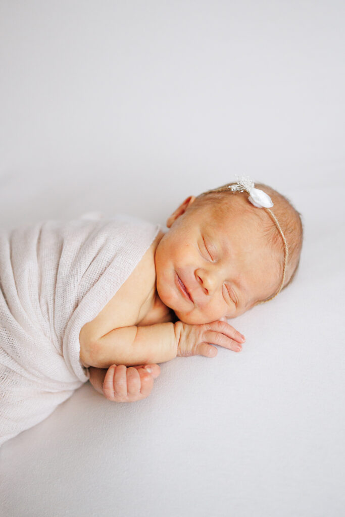 smiling newborn studio photo of baby girl wearing a simple flower headband in worthington Ohio newborn studio