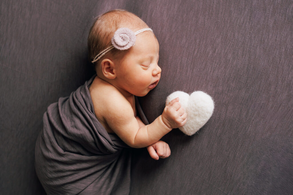 portrait of newborn baby girl in purple holding a white heart in worthington ohio newborn studio